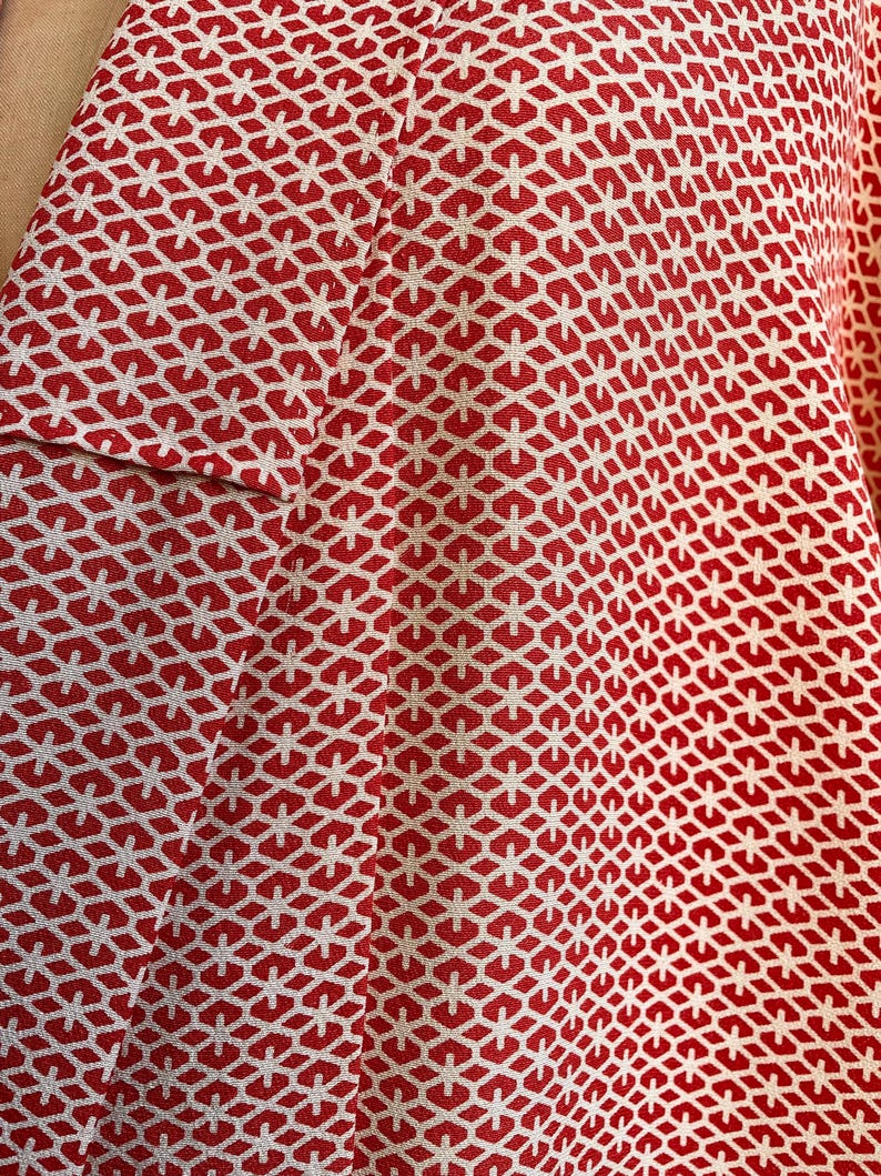 May include: Red fabric with a white geometric pattern. The pattern is made up of small hexagons and stars.