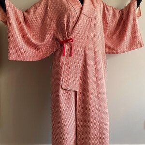 May include: A long, red and white patterned kimono with a red velvet sash. The kimono has a wide, flowing sleeve and a relaxed fit.