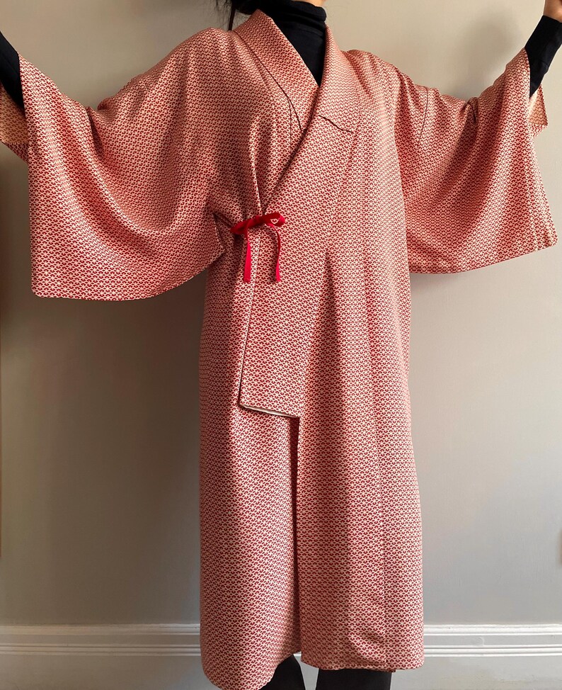May include: A long, red and white patterned kimono with a red velvet sash. The kimono has a wide, flowing sleeve and a relaxed fit.