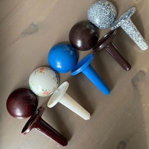 May include: A collection of decorative bottle stoppers in various colors and designs. Includes a white stopper with a floral design, a blue stopper, and stoppers in brown, white, and speckled gray. The stoppers are made of plastic and have a T-shaped design.