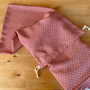 May include: Two red and white patterned fabric drawstring bags. The bags are made of a soft, lightweight fabric and have a simple design.