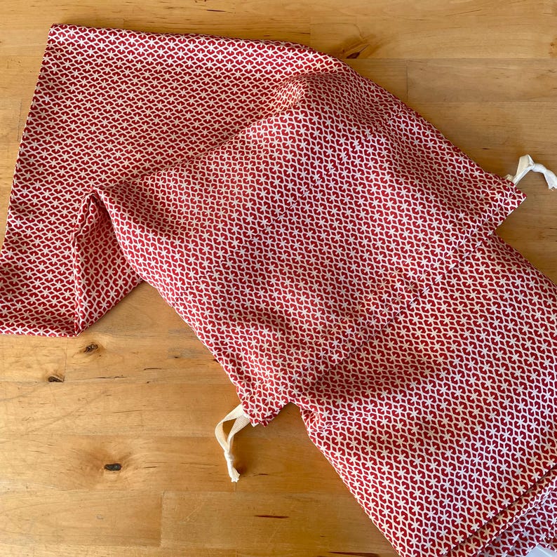May include: Two red and white patterned fabric drawstring bags. The bags are made of a soft, lightweight fabric and have a simple design.