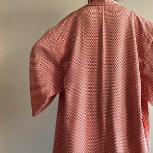 May include: A red and white patterned kimono with a long sleeve. The kimono has a small, repeating pattern of white flowers on a red background.