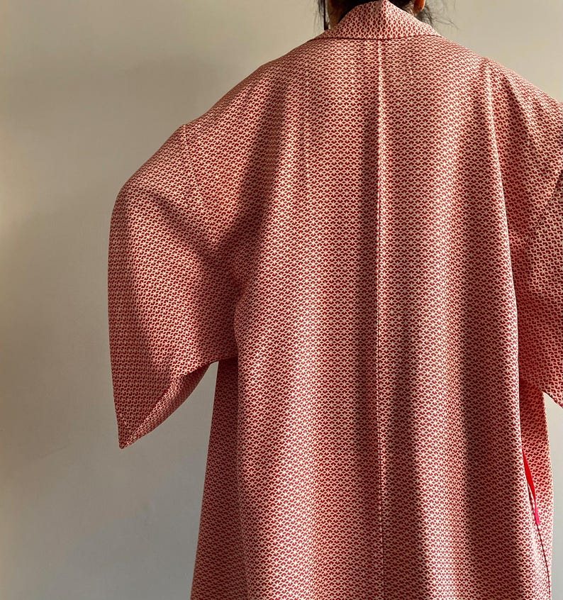 May include: A red and white patterned kimono with a long sleeve. The kimono has a small, repeating pattern of white flowers on a red background.