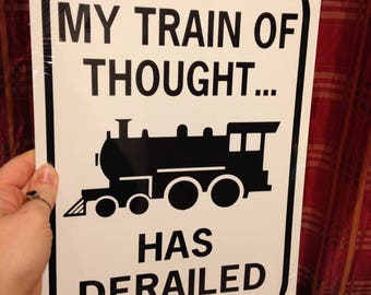 Può includere: Un cartello di metallo bianco con testo nero e una silhouette nera di un treno. Il cartello recita "Il mio treno del pensiero... è deragliato."