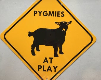 May include: Yellow diamond-shaped warning sign with black text and a silhouette of a goat. The sign reads "PYGMIES AT PLAY".