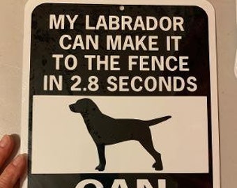 Op de afbeelding: Een zwart-wit bord met de tekst "My Labrador can make it to the fence in 2.8 seconds. Can you?" en een silhouet van een zwarte Labrador Retriever.