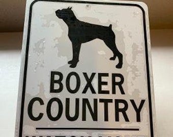 Op de afbeelding: Een wit bord met zwarte tekst en een zwart silhouet van een boxer. Het bord staat er "Boxer Country Watch Your Step!"