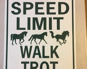 May include: White metal sign with green text that reads "Speed Limit Walk Trot Canter". Three black silhouettes of horses are shown in different gaits.