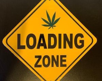Op de afbeelding: Een geel, ruitvormig bord met zwarte tekst dat "LOADING ZONE" aangeeft. Een groen marihuanablad bevindt zich in het bovenste midden van het bord.