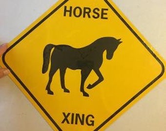 May include: Yellow diamond-shaped sign with black text and a black silhouette of a horse. The sign reads "HORSE XING".