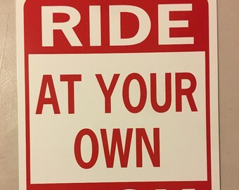 Op de afbeelding: Een rood en wit bord met de tekst "RIDE AT YOUR OWN RISK" in witte letters op een rode achtergrond.