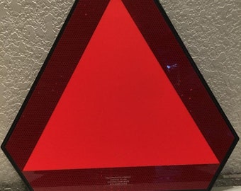 May include: Red reflective triangle shaped warning sign with black border. The sign has the text "TRAFFIC PRODUCTS COMPANY, MADE IN USA, DOT-FMVSS 125, 172448 E014" printed on the bottom.