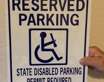 Op de afbeelding: Een wit bord met blauwe tekst die "Gereserveerd parkeren" zegt. Onder de tekst staat een blauw rolstoelpictogram. Het bord vermeldt ook "State Disabled Parking Permit Required".