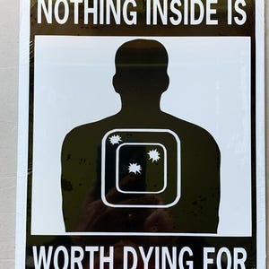May include: Black and white sign with a silhouette of a person with a target on their chest. The sign reads "NOTHING INSIDE IS WORTH DYING FOR."
