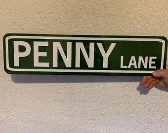 Op de afbeelding: Een groen metalen straatnaambord met witte letters met de tekst "PENNY LANE".