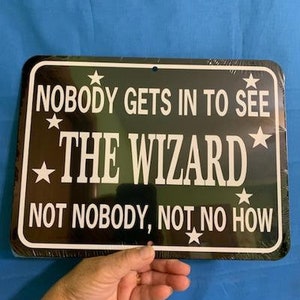 May include: Black metal sign with white text that reads "Nobody gets in to see The Wizard, Not nobody, not no how". The sign has five white stars around the text.