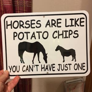 Puede incluir: Señal de metal blanco con texto negro y siluetas de caballos. La señal dice "Los caballos son como las patatas fritas, no puedes tener solo una."