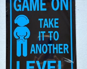 May include: Black metal sign with blue text and a gamer icon. The sign reads "GAME ON TAKE IT TO ANOTHER LEVEL". The gamer icon is a stick figure holding a game controller.