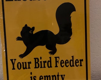May include: A yellow metal sign with black text and a black silhouette of a squirrel. The sign reads "Excuse me... Your Bird Feeder is empty."