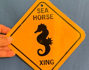 May include: A yellow diamond-shaped sign with black text and a black silhouette of a seahorse. The sign reads "SEA HORSE XING".
