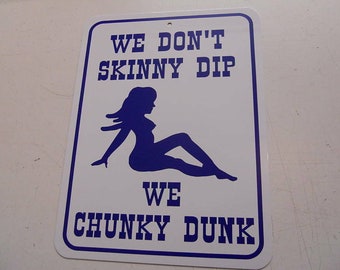 Op de afbeelding: Een wit metalen bord met blauwe tekst en een silhouet van een vrouw. Het bord luidt "We don't skinny dip, we chunky dunk."