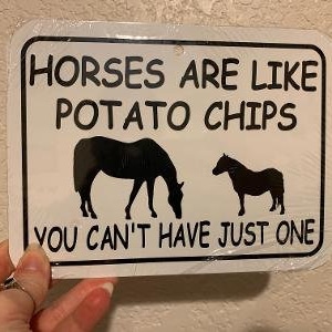 Puede incluir: Señal de metal blanco con texto negro y siluetas de caballos. La señal dice "Los caballos son como las patatas fritas, no puedes tener solo una."