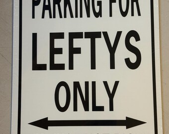 May include: A rectangular white metal sign with rounded corners and a black border. The text reads PARKING FOR LEFTYS ONLY in black capital letters. Below this is a black horizontal double-headed arrow and the text IT'S JUST NOT RIGHT.