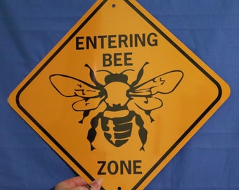 May include: Yellow diamond-shaped sign with black text and a black bee silhouette. The sign reads "Entering Bee Zone".
