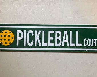May include: A green and white sign with the words "Pickleball Court" and a yellow pickleball.