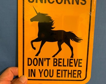 May include: A yellow metal sign with black text and a black silhouette of a unicorn. The sign reads "Unicorns Don't Believe In You Either."