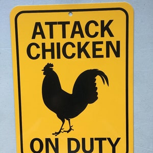 Puede incluir: Un cartel de advertencia amarillo con texto negro y una silueta negra de un gallo. El cartel dice "Attack Chicken On Duty".