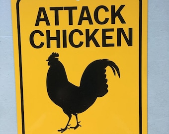 May include: Yellow warning sign with black text and a black silhouette of a rooster. The sign reads "Attack Chicken On Duty".