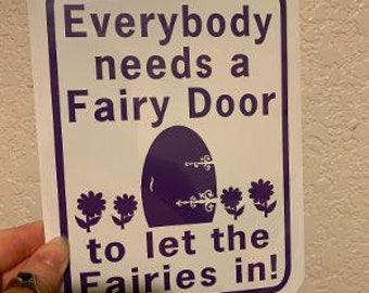 May include: White sign with purple text and a purple fairy door graphic. The sign reads "Everybody needs a Fairy Door to let the Fairies in!"