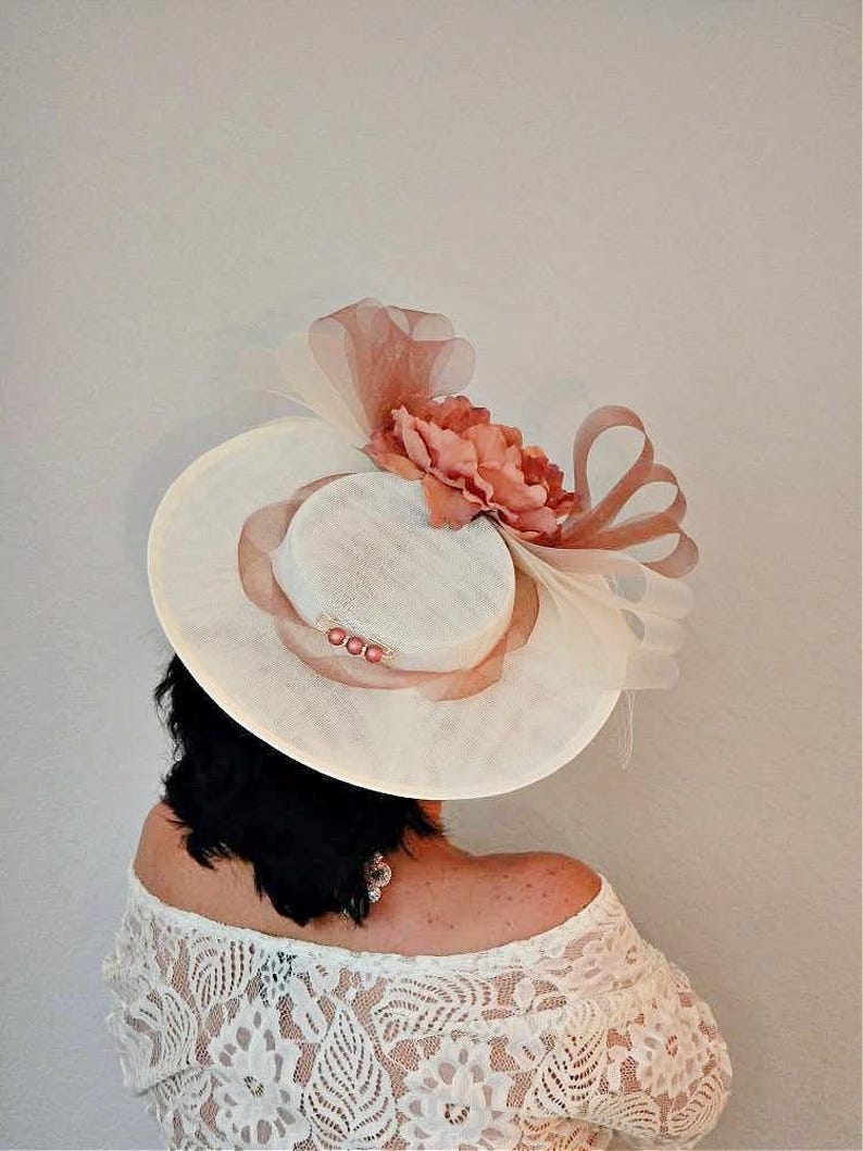Peut inclure: Un chapeau blanc &agrave; large bord avec un accent de fleur rose. Le chapeau est d&eacute;cor&eacute; d'un ruban rose et d'un petit groupe de perles.