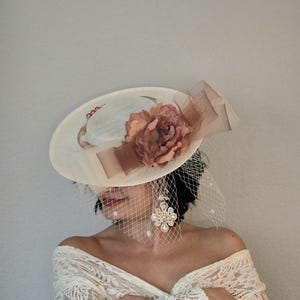 Peut inclure: Un chapeau blanc &agrave; large bord avec un accent de fleur marron. Le chapeau est d&eacute;cor&eacute; d'un voile transparent et d'un ruban marron. Le chapeau est port&eacute; par une personne aux cheveux longs et fonc&eacute;s et un haut en dentelle blanche.