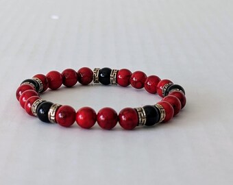 May include: A red and black beaded bracelet with silver accents. The bracelet is made of small, round beads and has a simple design.