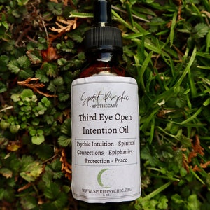 Op de afbeelding: Een bruine glazen fles met een zwarte druppelaar en een wit etiket. Het etiket luidt "Spirit Psychic - Apothecary - Third Eye Open Intention Oil - Psychic Intuition - Spiritual Connections - Epiphanies - Protection - Peace - WWW.SPIRITPSYCHIC.ORG - 2 oz."
