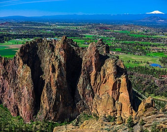 Puede incluir: Una vista panorámica de un paisaje rocoso con altas formaciones rocosas rojas en primer plano. El fondo presenta una cadena montañosa distante con un pico nevado.
