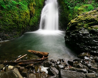 Könnte beinhalten: Ein Wasserfall stürzt über mit Moos bewachsenen Felsen in einen Wasserpool. Das Wasser ist klar und die Felsen sind dunkelgrau.