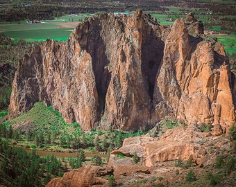 Puede incluir: Una vista en picado de una gran formación rocosa con lados escarpados y verticales. La roca es de color marrón rojizo y está rodeada de vegetación verde. Un pequeño río fluye por el valle debajo de la formación rocosa.