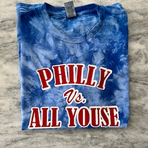 May include: A blue tie-dye t-shirt with the text "PHILLY vs. ALL YOUSE" in red.