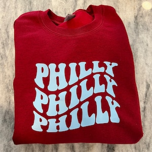 May include: A maroon sweatshirt with a light blue graphic that says "Philly" in a wavy, retro font.