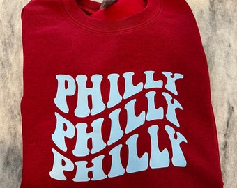 May include: A maroon sweatshirt with a light blue graphic that says "Philly" in a wavy, retro font.