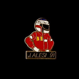 Peut inclure: Une épingle en émail rouge et blanche représentant un pilote de course de dessin animé portant un casque avec le mot "Marlboro" dessus. Le pilote se tient sur un rectangle noir avec le texte "J. ALESI. 91".