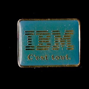 May include: A rectangular teal pin with a gold border. The pin displays the IBM logo in gold lettering and the phrase "C'est tout" in gold lettering below the logo.