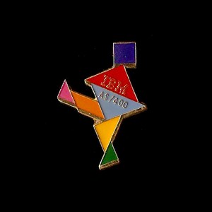 May include: A colourful IBM AS/400 pin with a geometric design. The pin features red, blue, yellow, green, and pink shapes, with the IBM logo and "AS/400" text. The pin has a gold border against a black background.