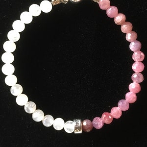 May include: A white and pink beaded bracelet with a silver clasp and a silver charm with the word "Mum" on it.