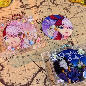 Puede incluir: Tres llaveros de plástico transparente con ilustraciones de personajes de estilo anime de colores. Los llaveros tienen el texto "Fleeting Lullaby", "Bink's Sake" y "Bink's Sake".