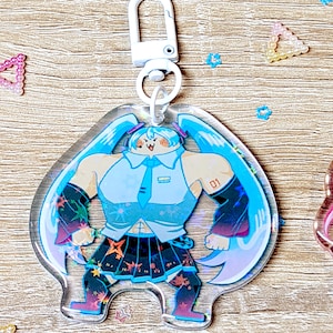 Puede incluir: Un llavero de acr&iacute;lico transparente con un personaje de dibujos animados con cabello azul, una camisa blanca, una falda negra y botas blancas y negras. El personaje est&aacute; de pie con los brazos extendidos y tiene una expresi&oacute;n juguetona en su rostro. El llavero tiene un anillo de metal plateado y un clip de pl&aacute;stico blanco.